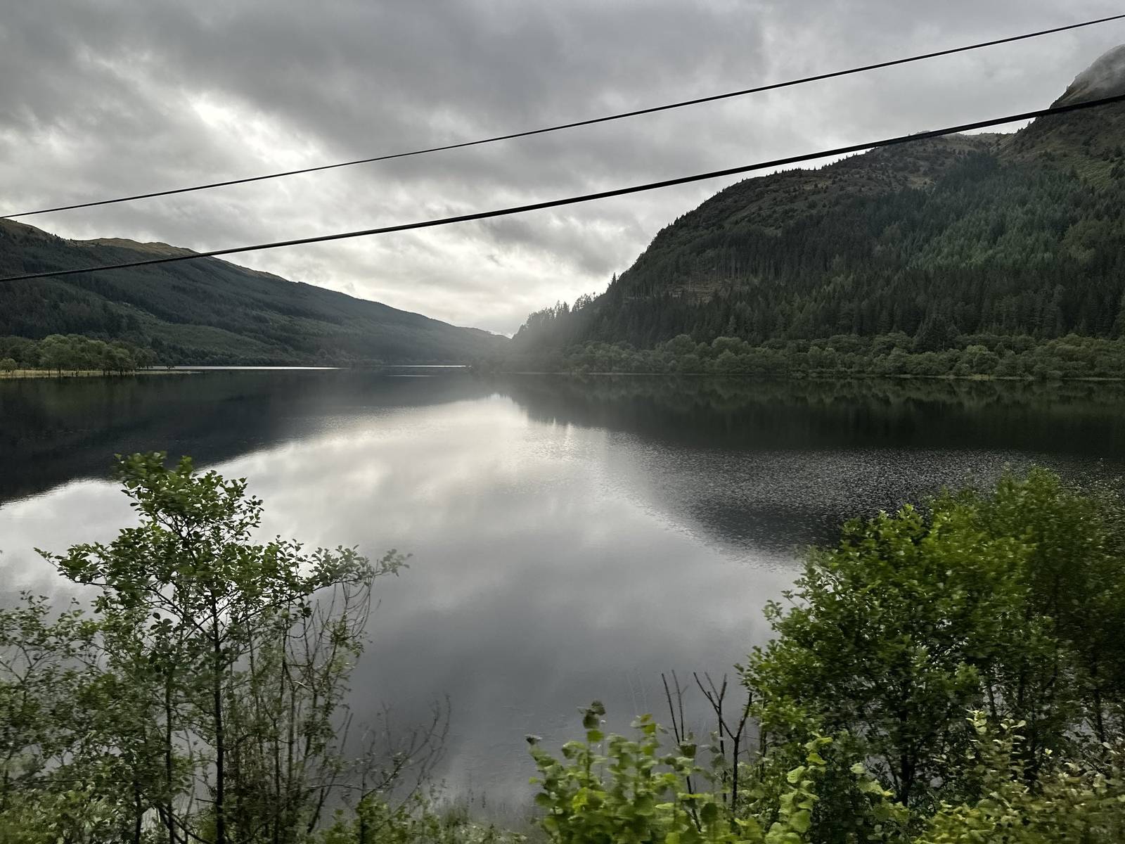 A still loch reflecting wooded hills